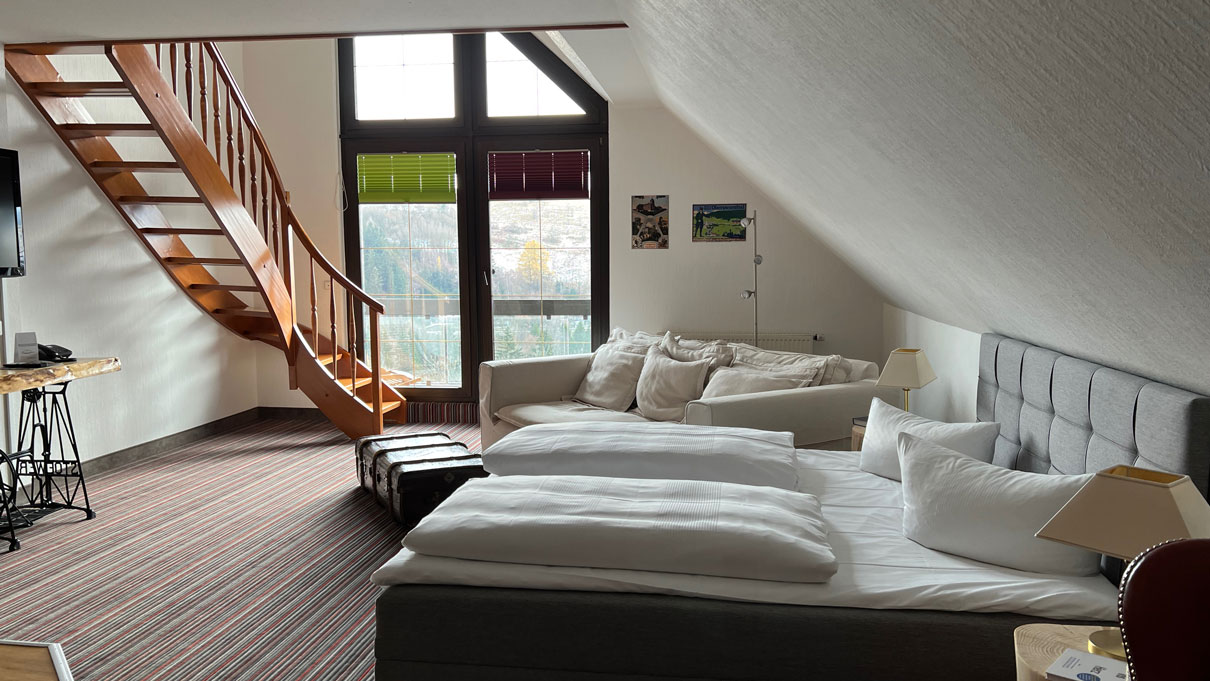 Gesamtansicht Zimmer mit Doppelbett, Fenster und Treppenaufgang