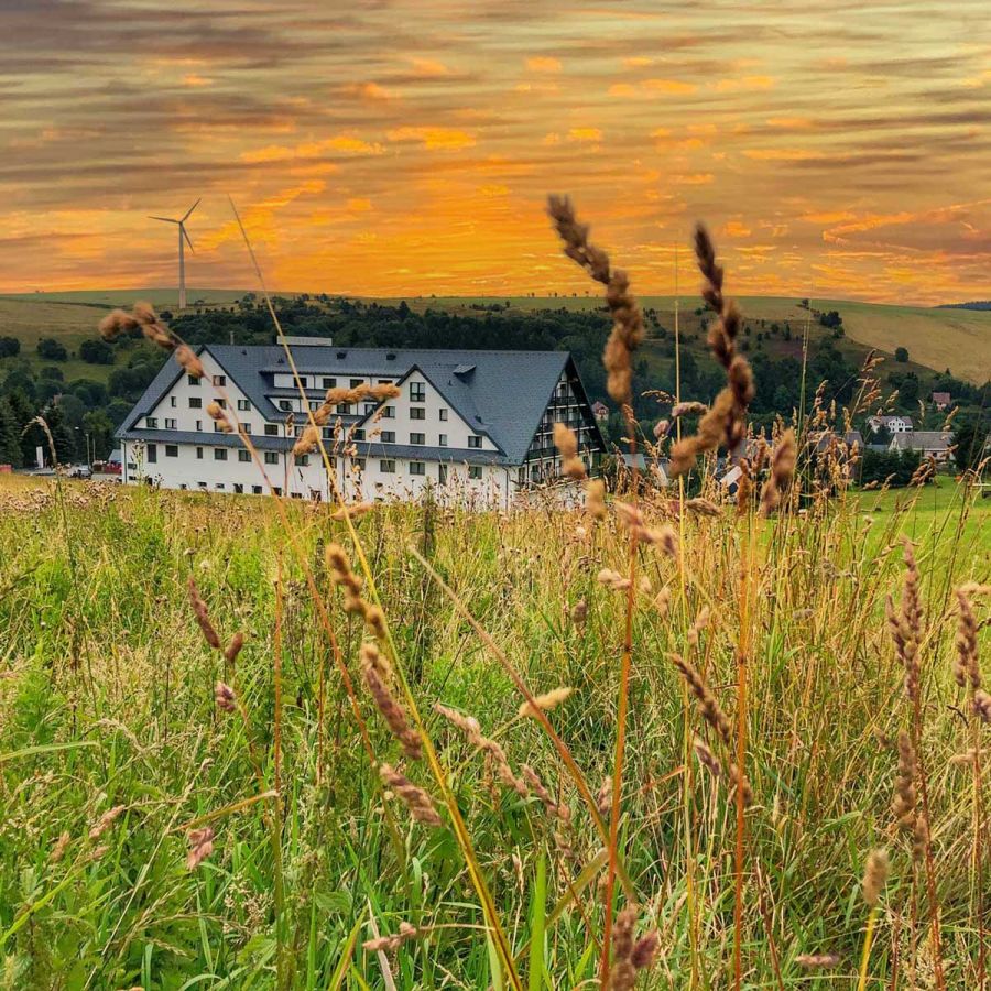 Alpina-Lodge Außenansicht im Hintergrund von Wiese, Sonnenuntergang