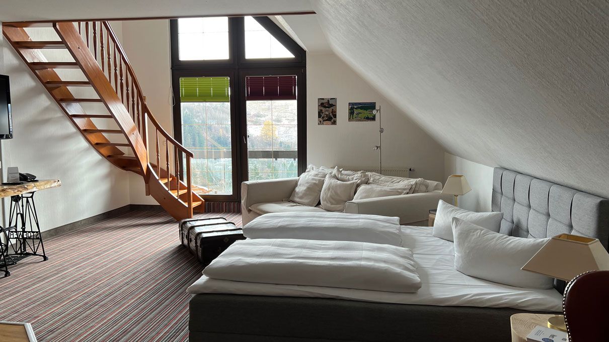 Gesamtansicht Zimmer mit Doppelbett, Fenster und Treppenaufgang